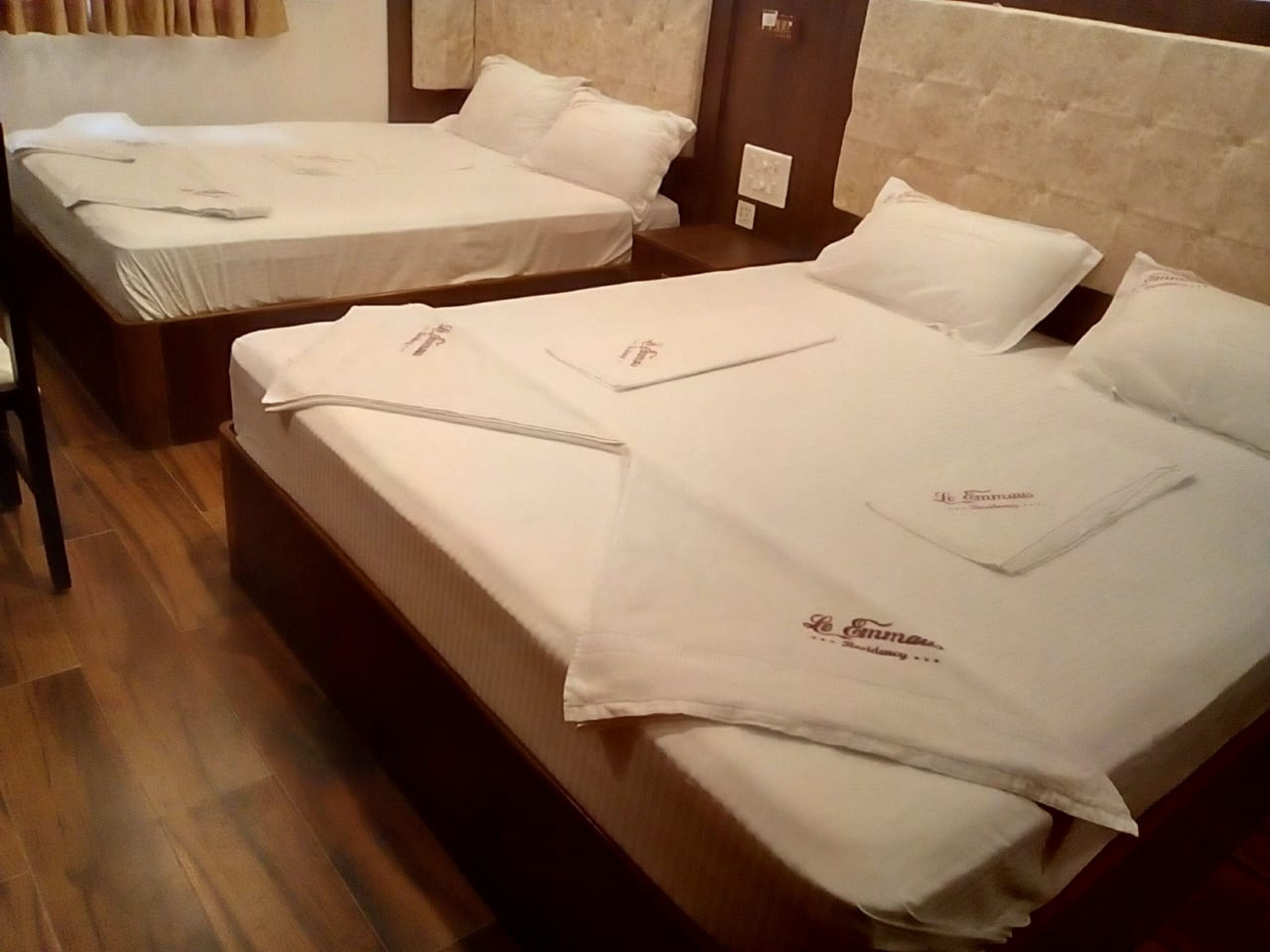 Habitación de hotel con dos camas, cada una con sábanas y almohadas blancas, y suelo de madera.