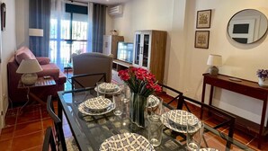 Un coin repas avec une table en verre dressée pour quatre personnes, un canapé, un téléviseur et un meuble en arrière-plan.