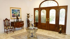 A grand foyer with a large wooden door, a decorative vase, a chair, and a painting on the wall.