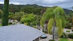A residential area with a house featuring a tiled roof, a garden with various plants, and a view of a hilly landscape in the background.