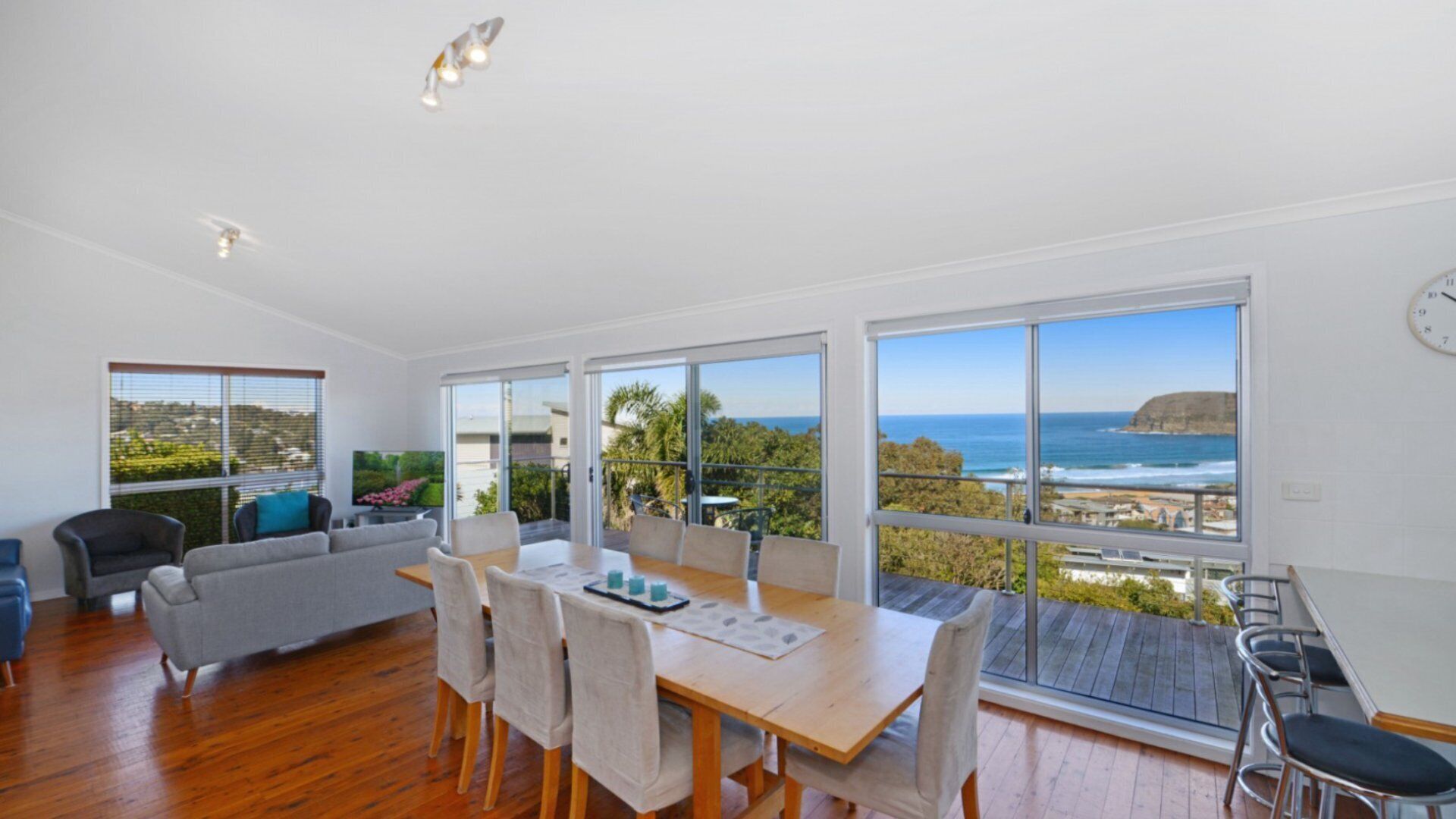 A spacious living room with a large dining table, comfortable seating, and a view of the ocean.