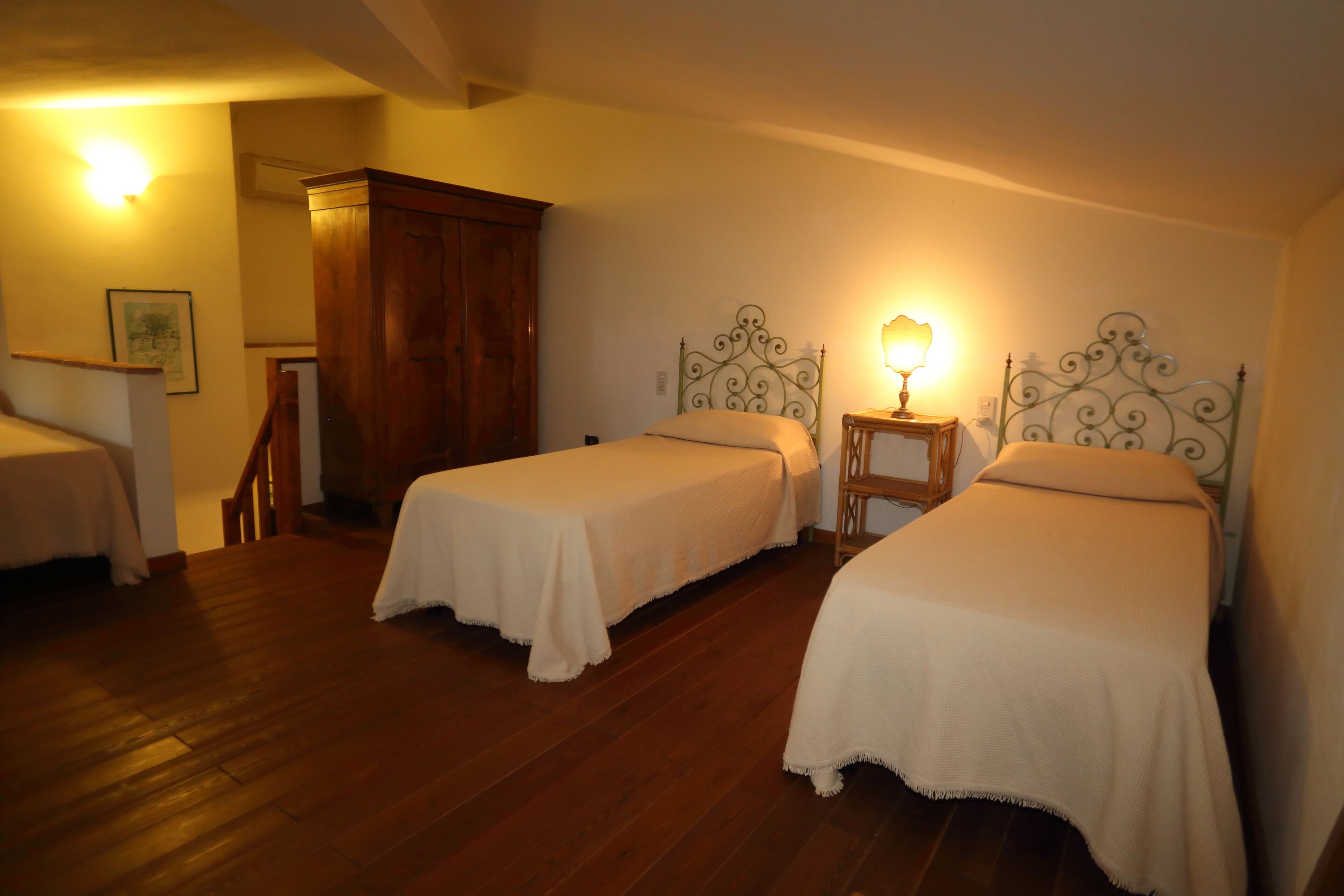 Une chambre avec deux lits simples, un plancher en bois, une armoire en bois et une petite table avec une lampe.