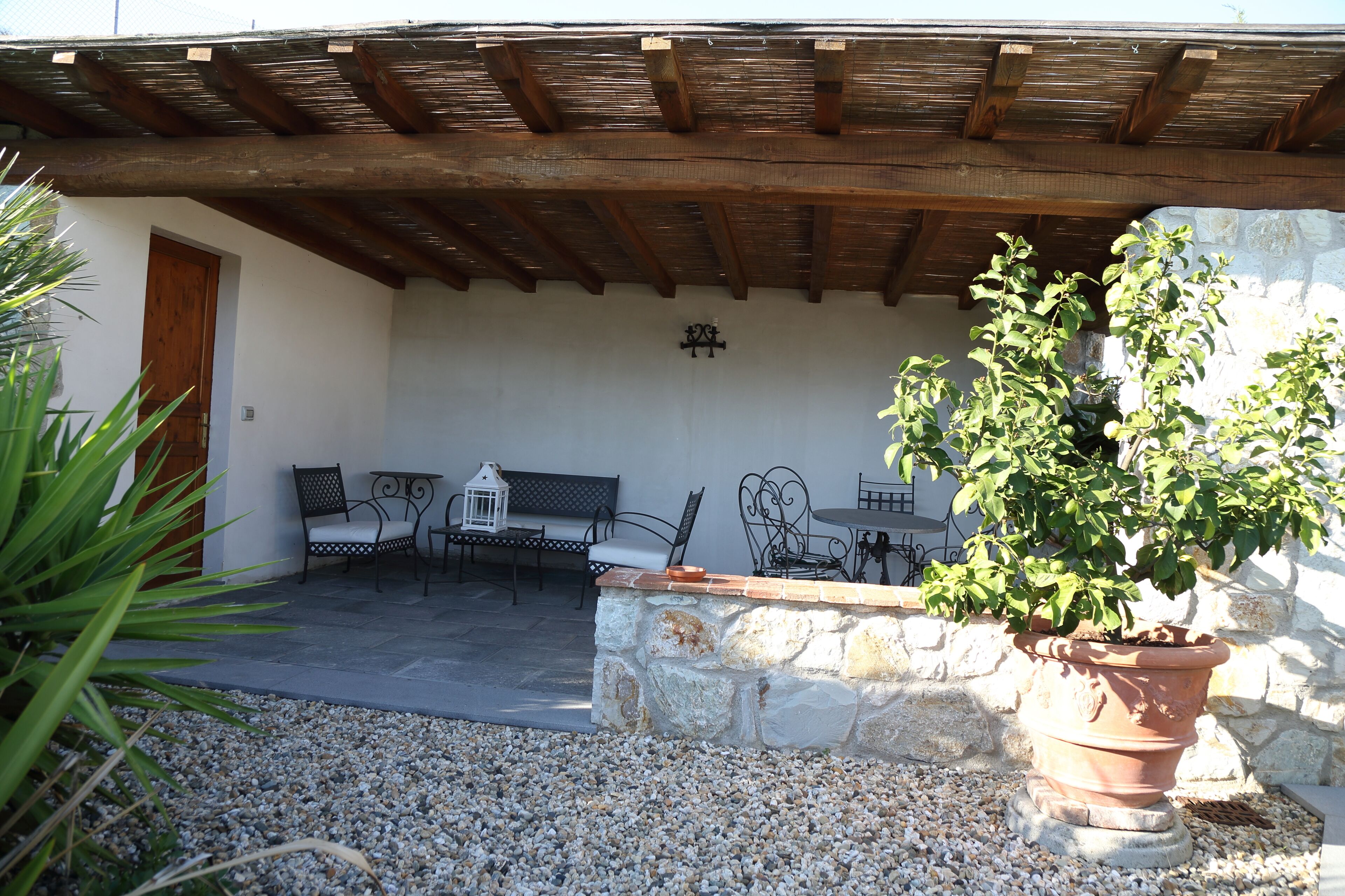 Une terrasse extérieure dotée d’un sol en pierre, d’une pergola en bois et d’un espace détente avec des chaises et une table en métal.