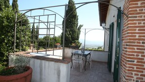 Un patio con una mesa y sillas, una planta grande en maceta y vistas al mar.
