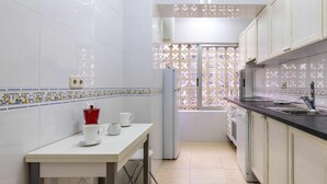 A kitchen with white tiled walls, a window with a decorative screen, a white countertop, and a sink.