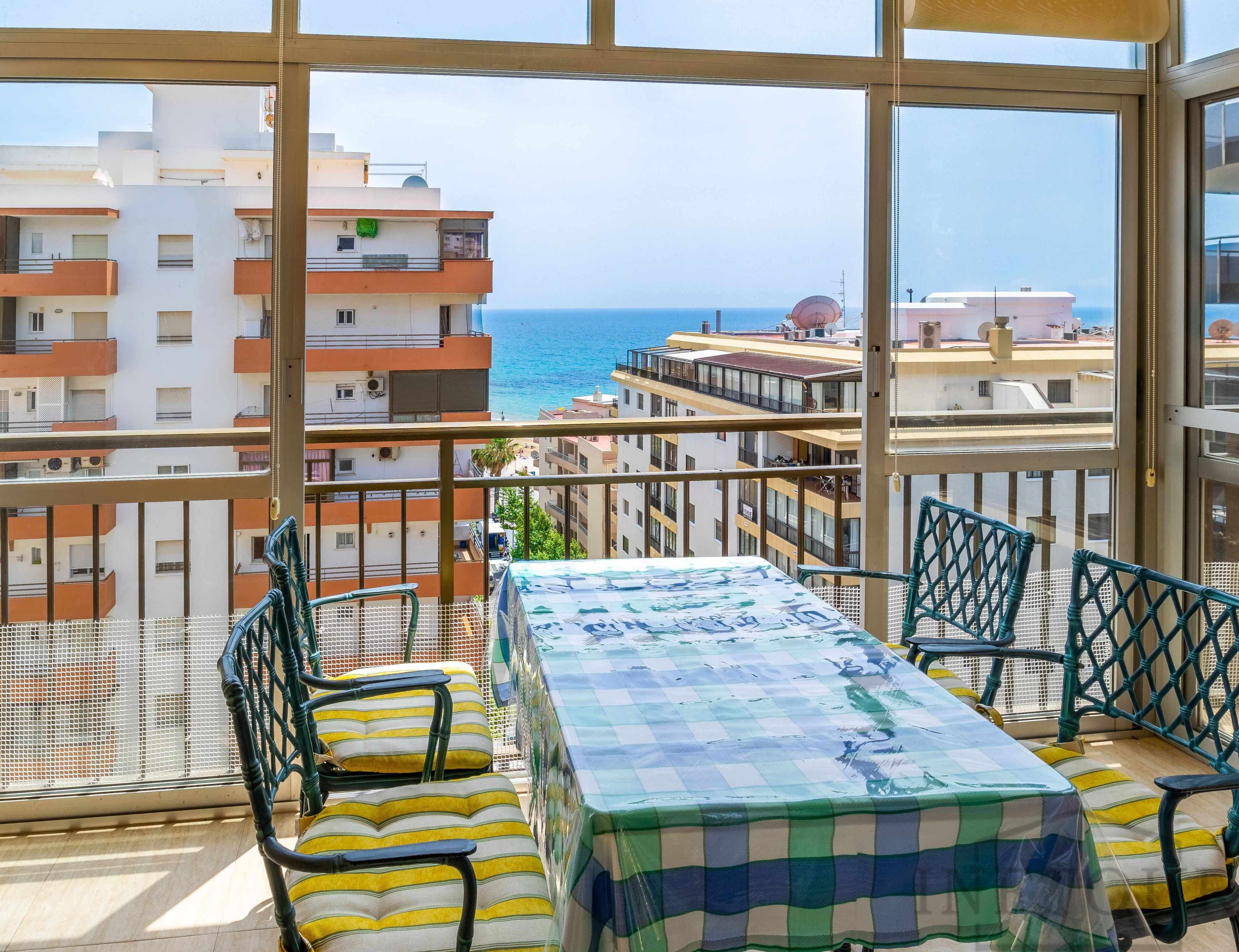 A balcony with a table and chairs, overlooking a coastal cityscape.