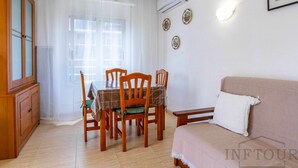 A room with a dining table, chairs, a sofa, a cabinet, and a wall-mounted air conditioner.