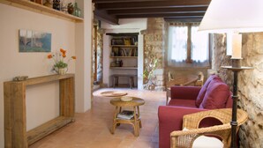 A cozy living room with a red sofa, wicker chairs, a wooden console table with a vase of flowers, and a bookshelf. - More Riera SPECTACULAR FARMHOUSE near Besalú for 13 people (Maià de Montcal)