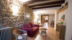 A cozy living room with a stone wall, a red sofa, wicker chairs, a small round table, and a wooden console table with decorative items. - More Riera SPECTACULAR FARMHOUSE near Besalú for 13 people (Maià de Montcal)