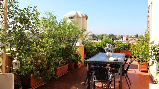 Eine Terrasse mit Tisch und Stühlen, umgeben von Blumentöpfen und einer kleinen Turmstruktur.