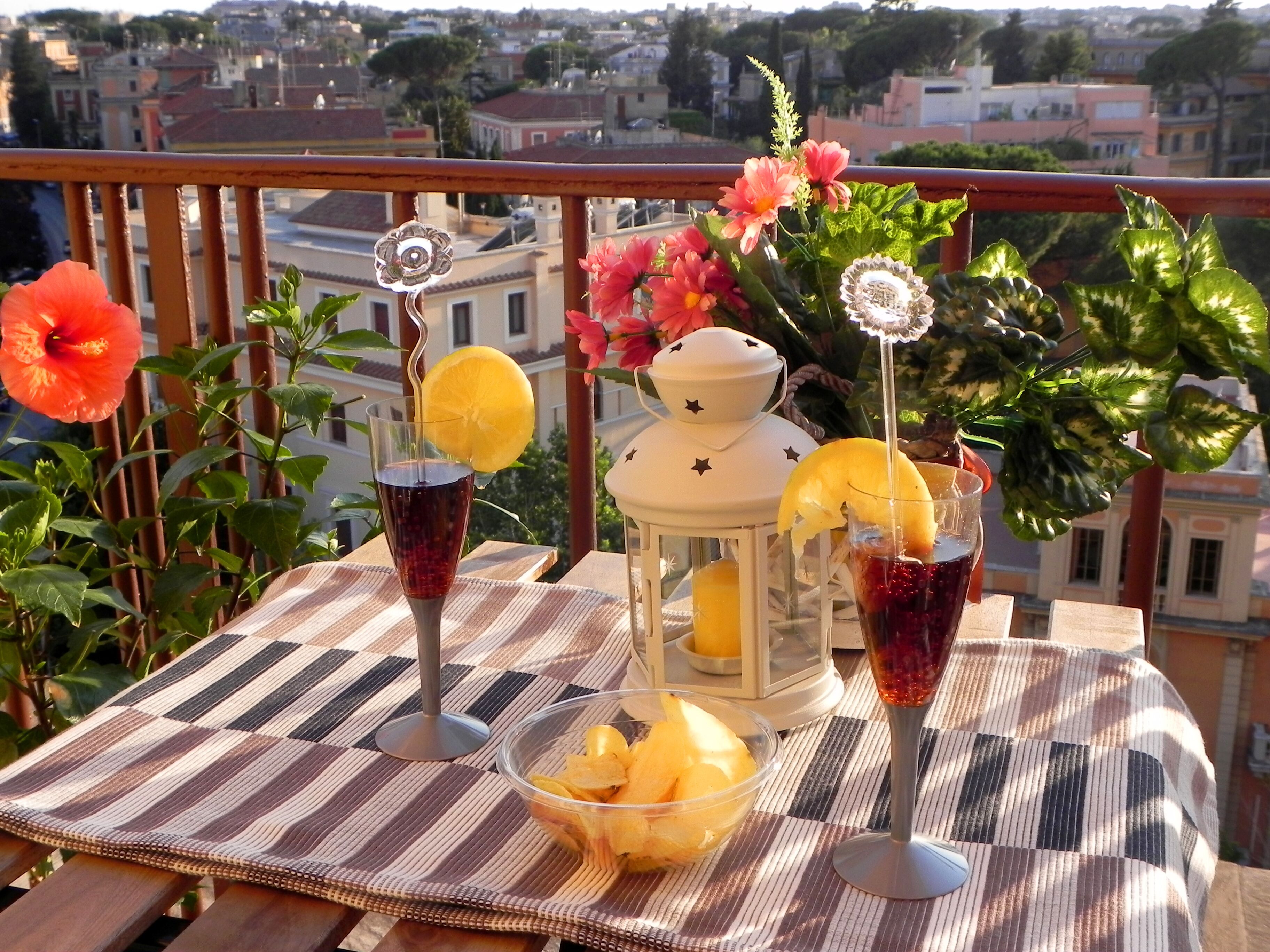 A balcony with two drinks, a lantern, and a bowl of fruit.