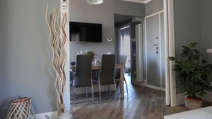 Ein moderner Essbereich mit an der Wand montiertem Fernseher, einem Esstisch mit Stühlen und einer Pflanze rechts.