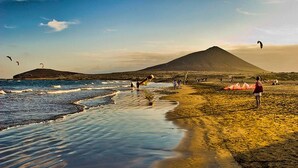 A beach with a mountain in the background, people flying kites, and a calm sea. - Hot Tub, sea, wifi pro, gas barbecue, garden, 11 (San Miguel de Abona)