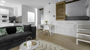 Ett modernt vardagsrum med en mörkgrå soffa, ett vitt matbord och en liten köksdel.