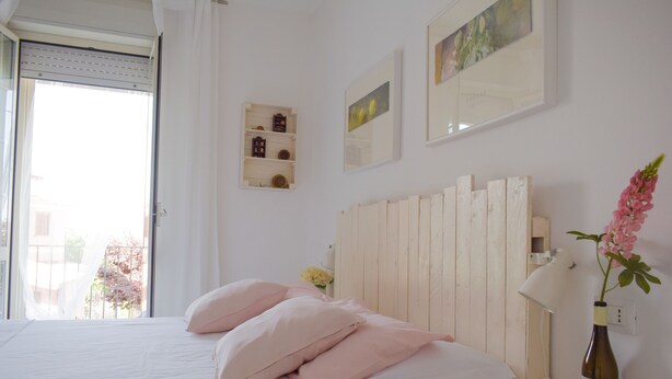 A bedroom with a bed, a bedside table, a lamp, and a bottle of wine.