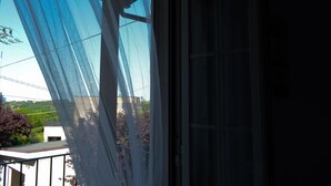A view from a balcony with a mesh screen, overlooking a building and greenery.
