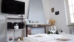 A modern hotel room with a flat-screen TV, a fireplace, a dining area with a table set for two, and a window with a view.