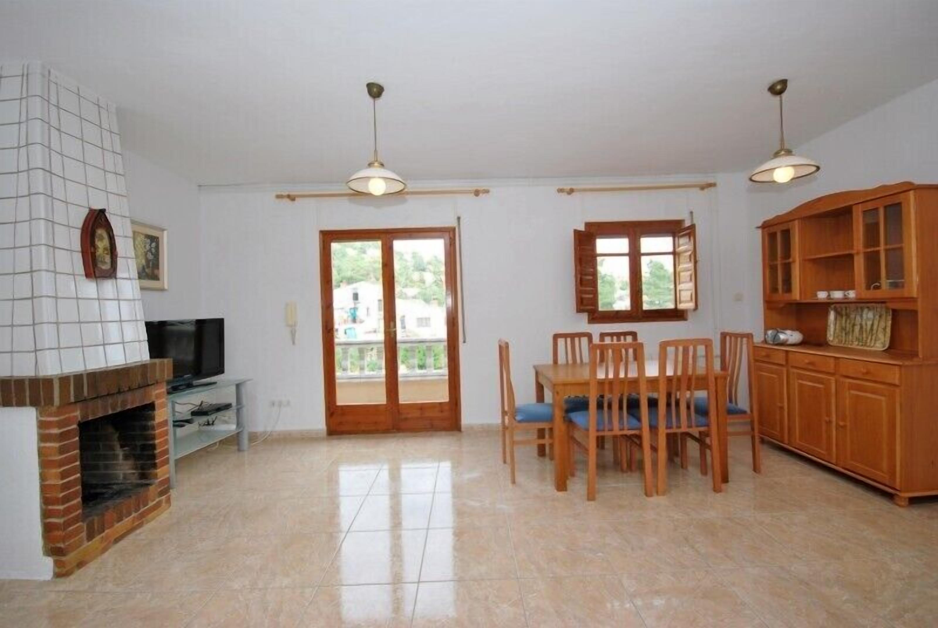 A spacious living area with a fireplace, a dining table with chairs, a television, and wooden cabinets.