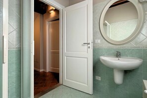 Une salle de bain avec une porte blanche, un lavabo avec un miroir et des murs recouverts de carreaux verts.