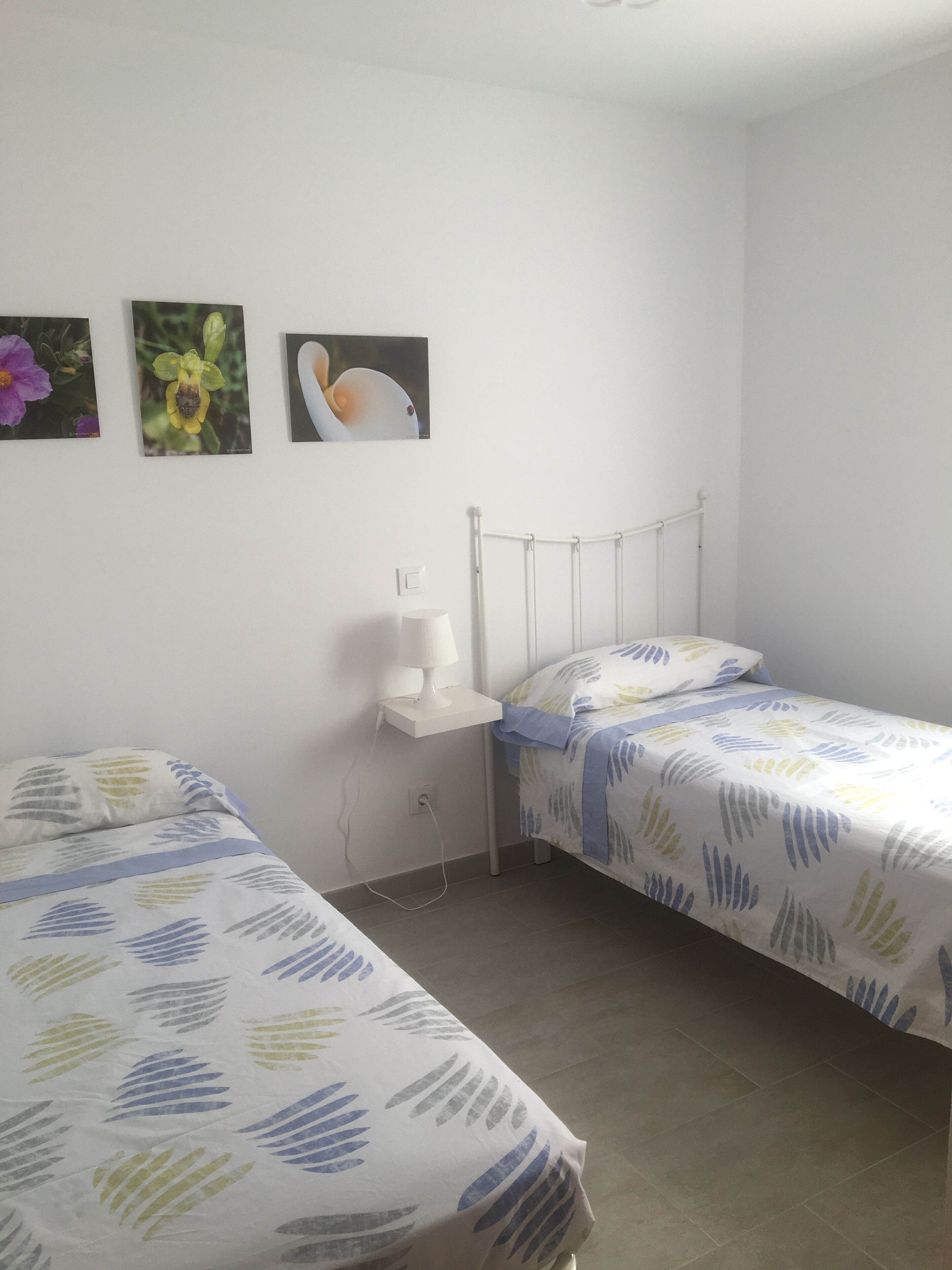 Ein kleines, sauberes Zimmer mit zwei Einzelbetten, einem Nachttisch mit Lampe und drei Wandbildern.