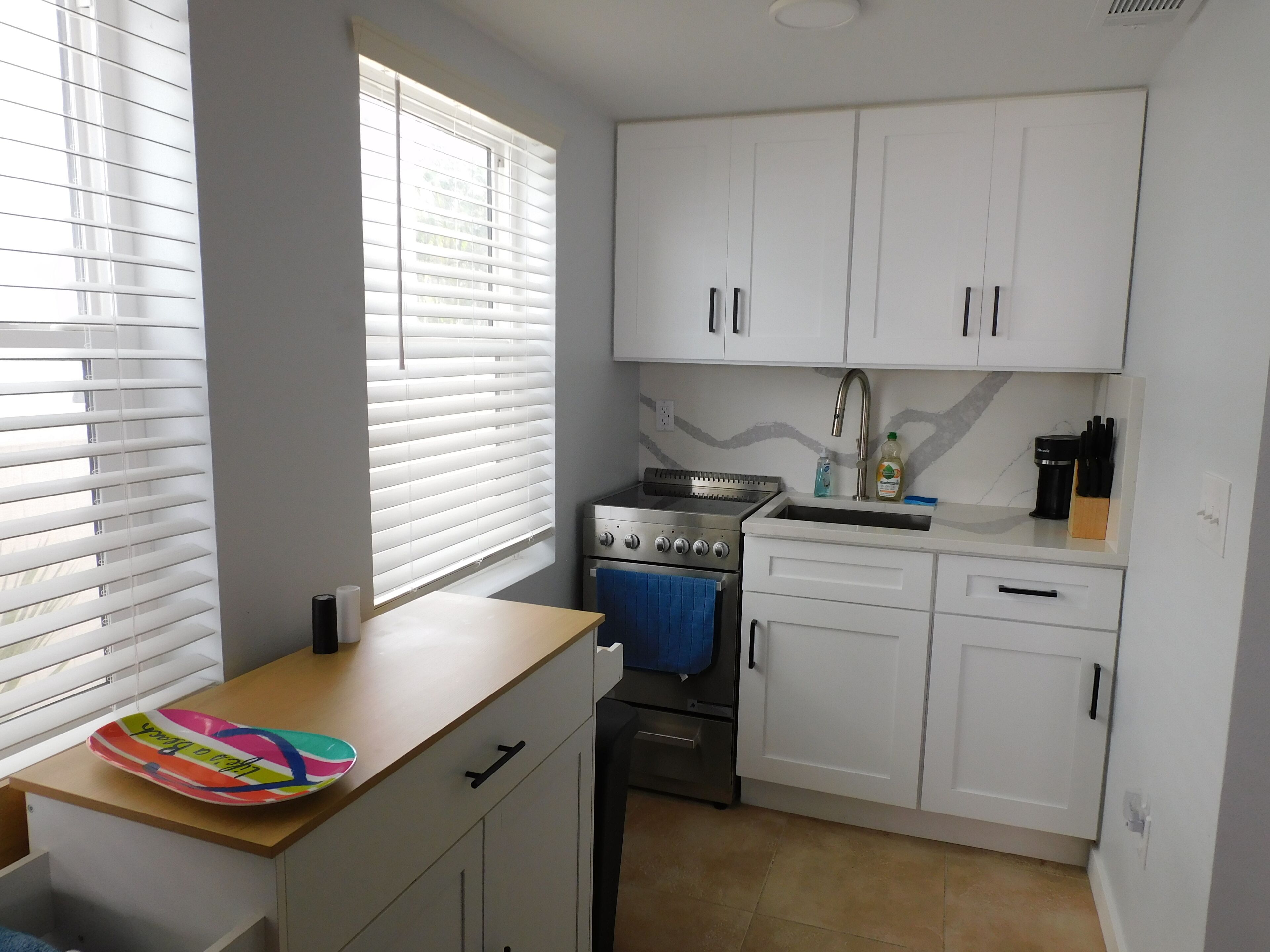 A compact kitchen with white cabinets, a stove, and a sink.