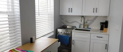 A compact kitchen with white cabinets, a stove, and a sink.