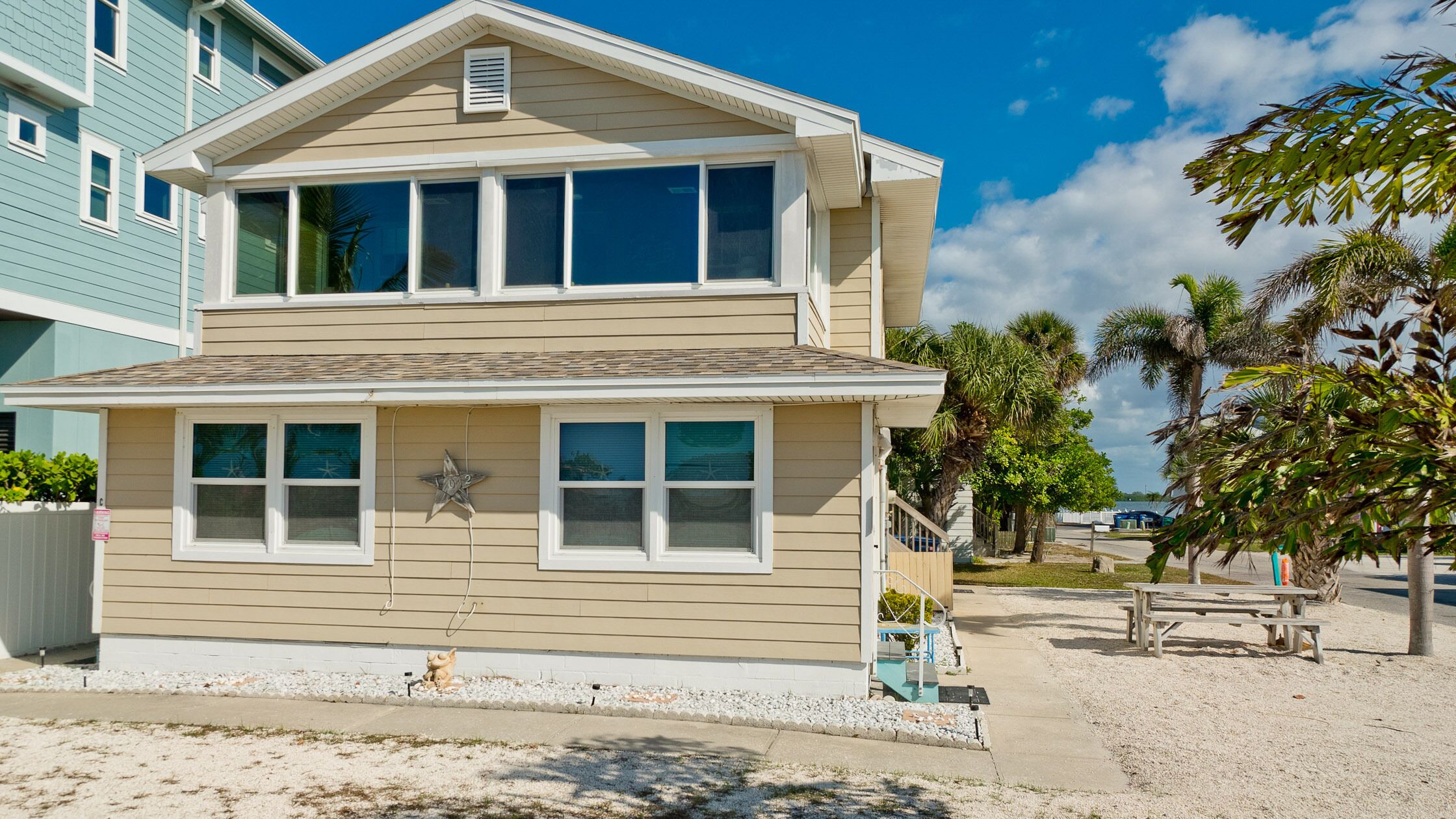 A two-story beach house with a star decoration, a small porch, and a sandy front yard.