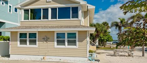 A two-story beach house with a star decoration, a small porch, and a sandy front yard.