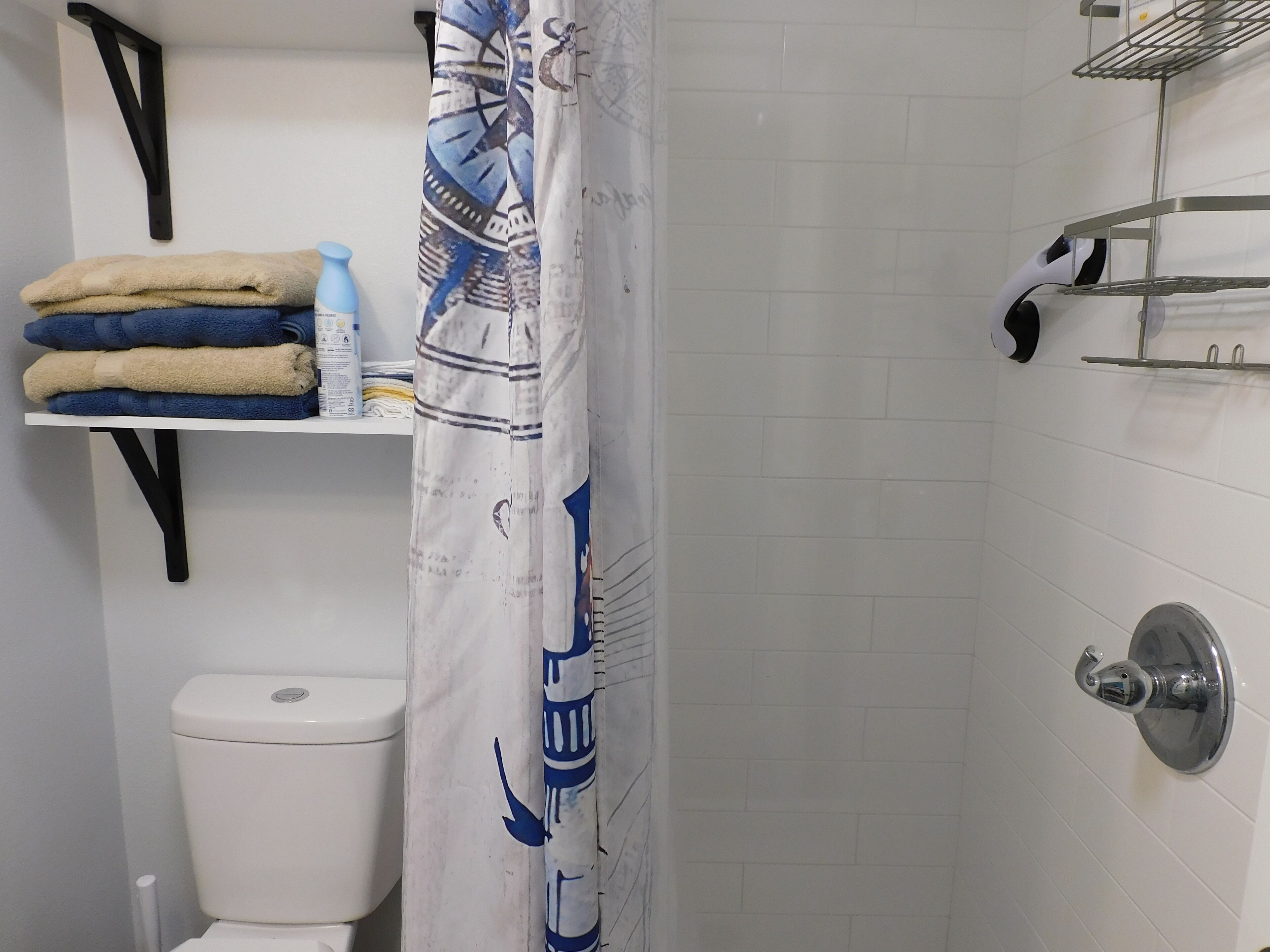 Une salle de bain comprenant des toilettes, une étagère avec des serviettes pliées, un rideau de douche et une autre étagère avec des articles de toilette.