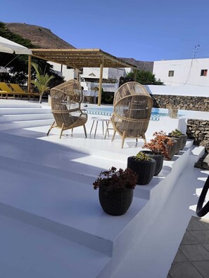Un espace piscine aménagé sur le toit, avec des fauteuils en osier, une pergola et des plantes en pot.