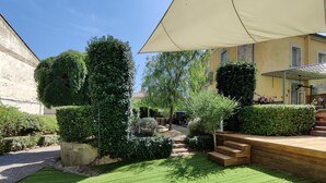 A courtyard with neatly trimmed hedges, a wooden deck, and a large umbrella providing shade. - Charming wine maker house with generous surfaces, garden and pool in Languedoc (Murviel-Lès-Béziers)