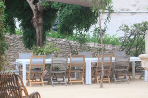 Un espace de restauration en plein air avec un mur en pierre, des chaises en bois et une table blanche.