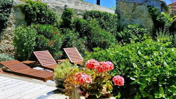 A wooden deck with lounge chairs, a stone wall, and lush greenery. - Charming wine maker house with generous surfaces, garden and pool in Languedoc (Murviel-Lès-Béziers)