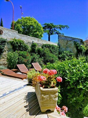 Una terraza de madera con sillas de descanso, un muro de piedra y abundante vegetación.