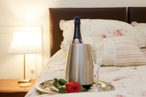 A champagne bottle on a tray with a glass and a rose on a bed with floral bedding and a nightstand with a lamp. - Annie's Cottage.  A pretty chocolate box style cottage with lots of character. (Kent)