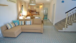 A living room with a beige sofa, patterned floor tiles, and a staircase. - BLUE BAY HOUSE (Marina San Gregorio)