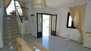 A living room with a sofa, a staircase, and a view through an open door. - BLUE BAY HOUSE (Marina San Gregorio)