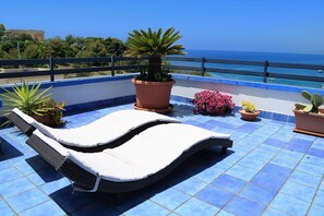 Une terrasse sur le toit avec deux chaises longues, des plantes en pot et une vue sur la mer.