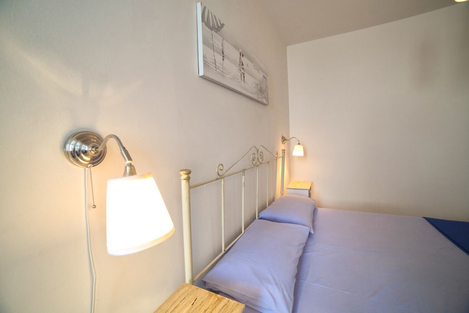 A bedroom with a bed, two bedside lamps, a wall-mounted light fixture, and a framed picture.