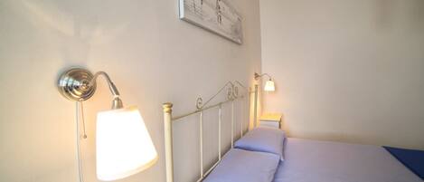 A bedroom with a bed, two bedside lamps, a wall-mounted light fixture, and a framed picture.
