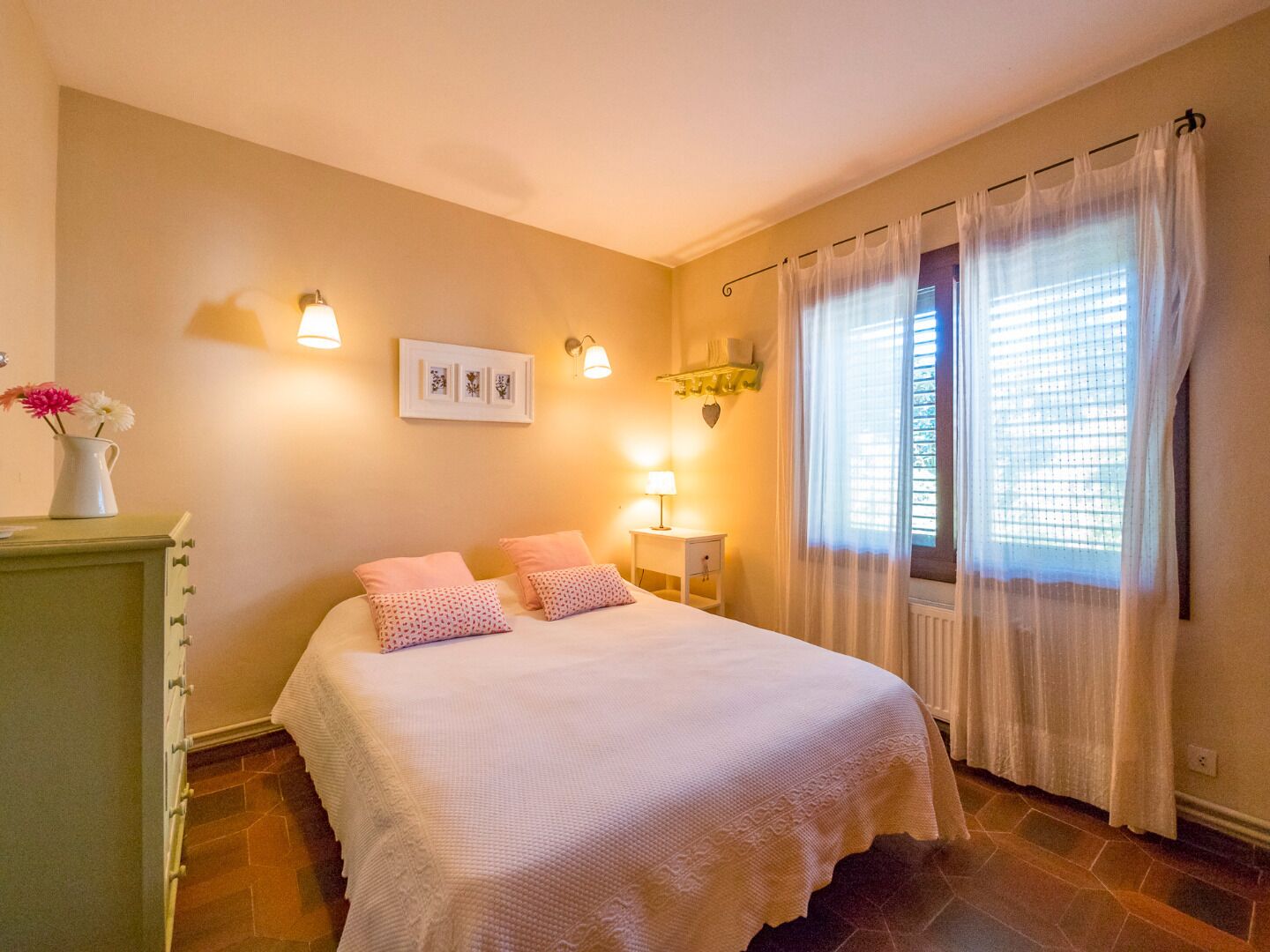 A bedroom with a bed, bedside tables, a dresser, and a window with curtains.