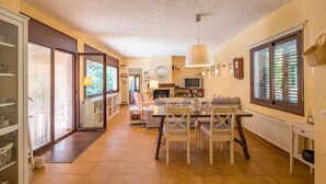 Zona d'estar àmplia amb taula de menjador, cadires, sofà i llar de foc. Es veu una cuina al fons.