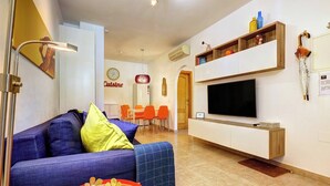 A modern living room with a sofa, TV, and a dining area in the background.