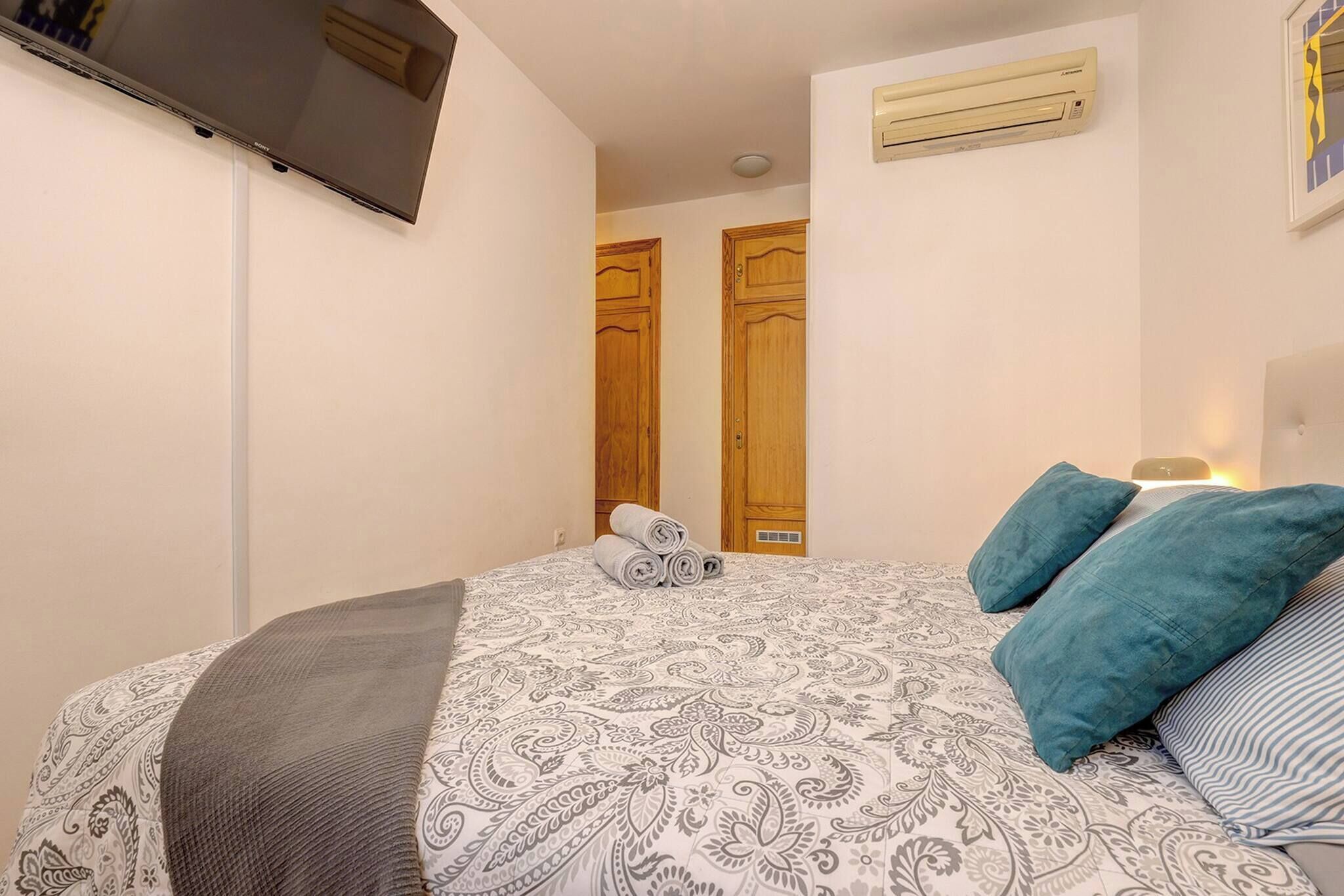 A bedroom with a bed, a TV mounted on the wall, and two wooden doors.