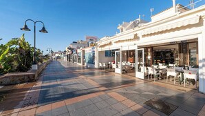 A pedestrian street with outdoor seating, shops, and a clear blue sky.