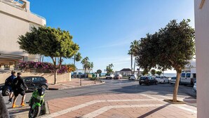 A street view with a green motorcycle parked on the sidewalk, a pedestrian crossing, and a row of parked cars and vans.