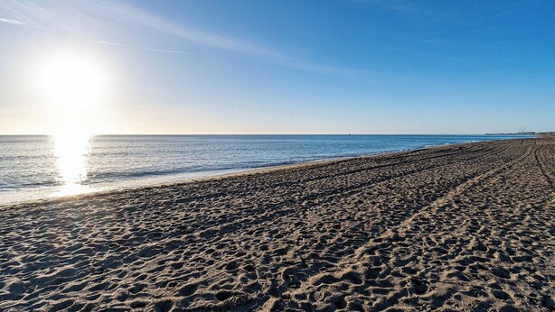 A beach with a clear sky and the sun shining on the sand.