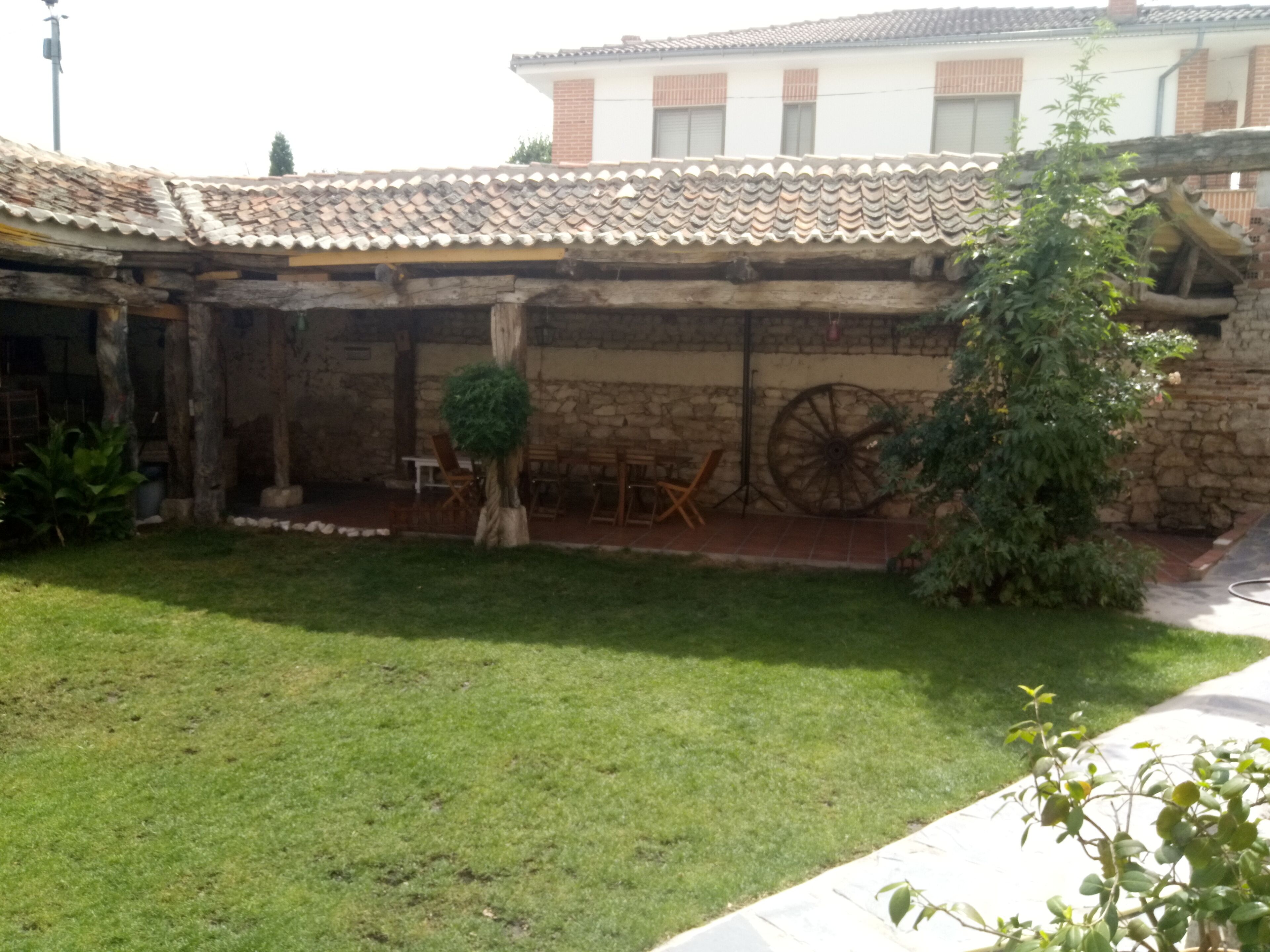 Un cortile con un muro in pietra, un tavolo di legno e una ruota.