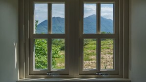Een uitzicht op bergen en groen vanuit een raam.