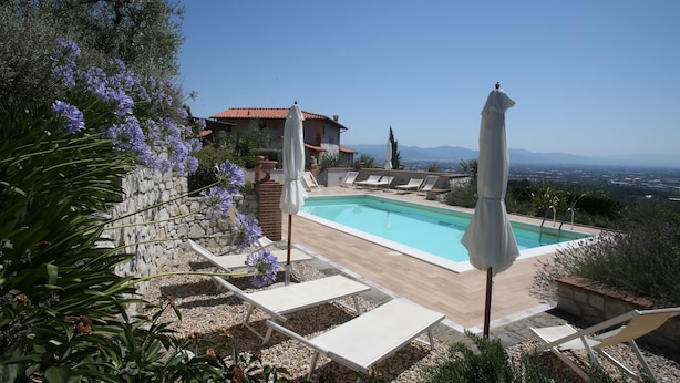 A pool area with lounge chairs and umbrellas, surrounded by stone walls and vegetation.